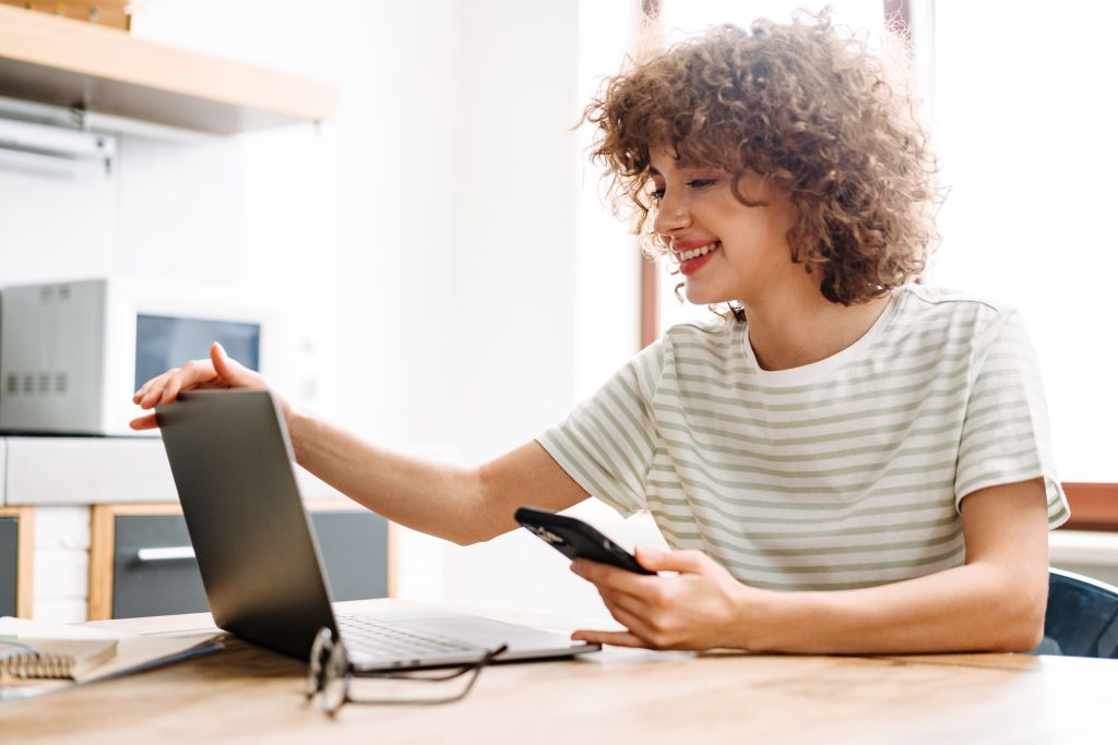 Chica de pelo rizado con la mano apoyada en un portátil preparada para hacer formación online