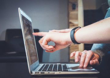 Dos personas trabajando sobre un portátil. Una de ellas indica un elemento sobre la pantalla mientras la otra controla el trackpad.