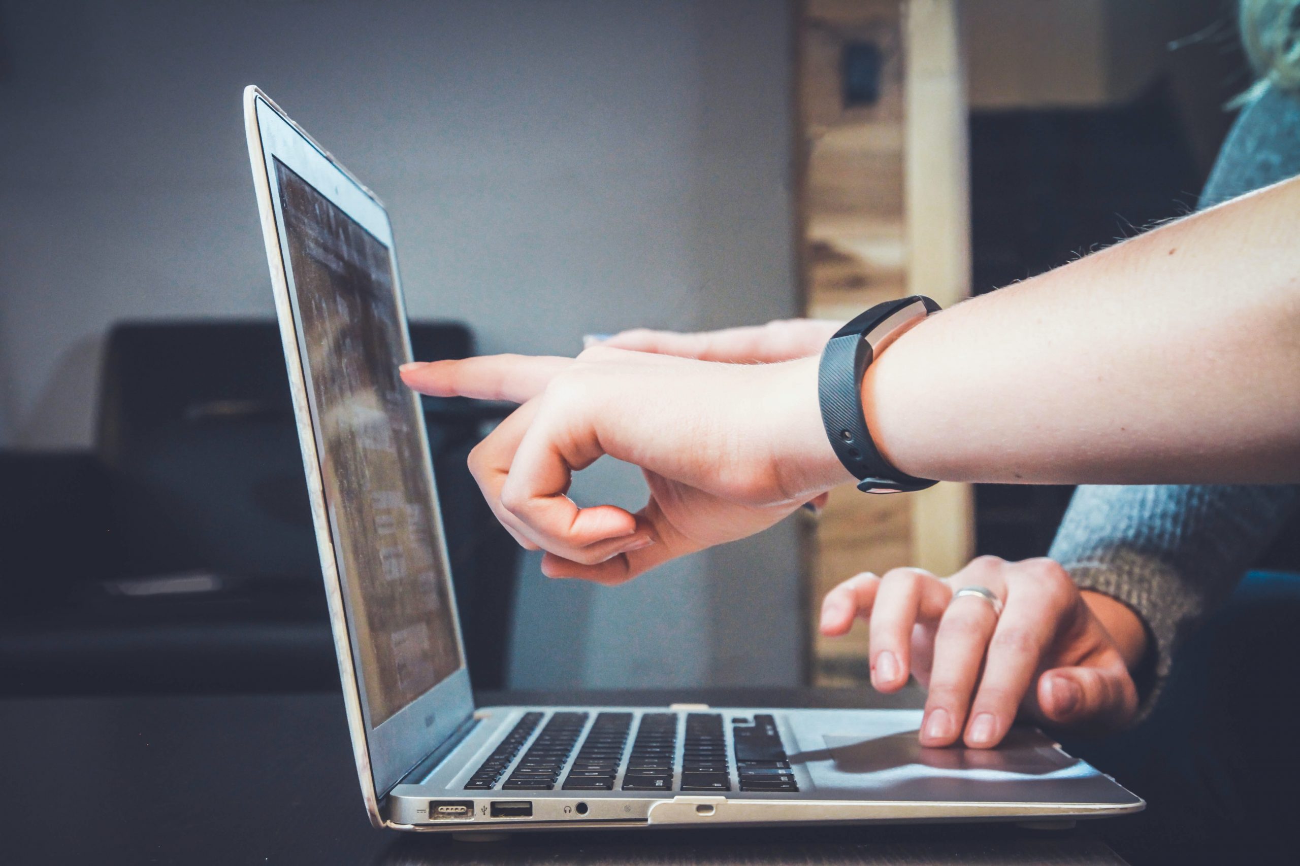 Dos personas trabajando sobre un portátil. Una de ellas indica un elemento sobre la pantalla mientras la otra controla el trackpad.