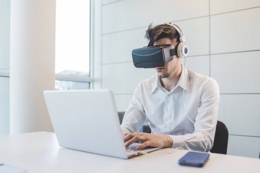 Chico con gafas de realidad virtual y ordenador portátil aprendiendo en el metaverso