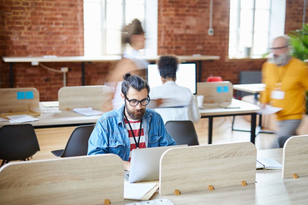 Hombre de negocios serio en ropa informal sentado junto al escritorio delante del portátil y analizando datos en línea o haciendo páginas web en la oficina.